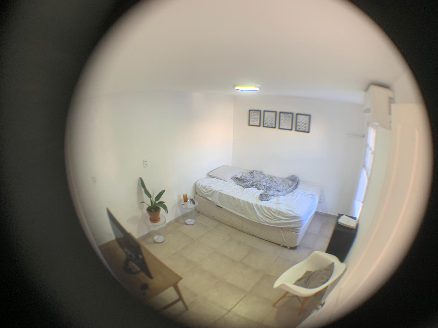 Foto circular olho de peixe de um quarto branco com cama, televisão e decorações simples