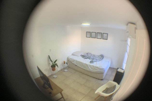 Foto circular olho de peixe de um quarto branco com cama, televisão e decorações simples