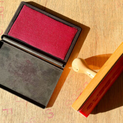 Almofada de tinta vermelha com carimbo escrito "Foi Deus" sob uma mesa de madeira