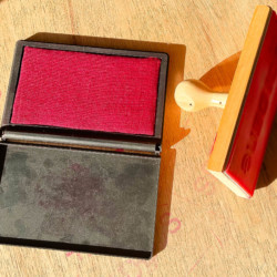 Almofada de tinta vermelha com carimbo escrito "Foi Deus" sob uma mesa de madeira