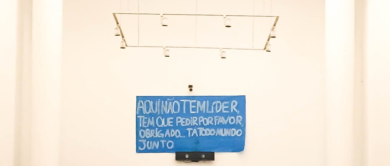 Foto de parede com papéis colados com frases, sendo uma delas "Aqui não tem líder, tem que pedir por favor, obrigado... Tá todo mundo junto."